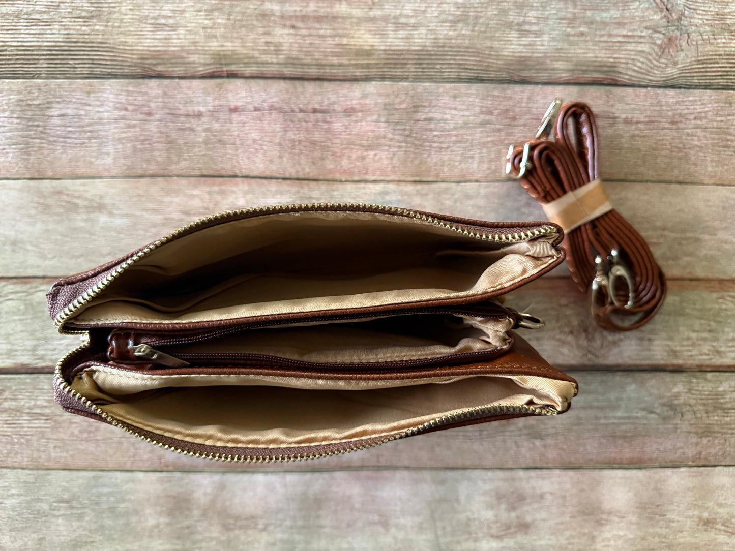 Brown leather clutch bag with a strap on a wooden surface