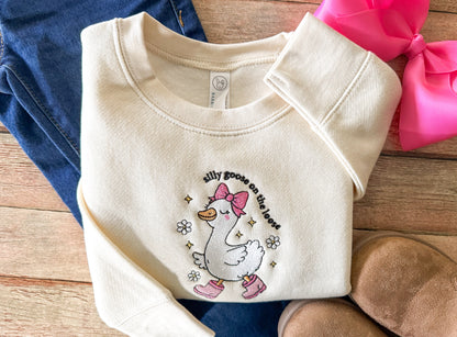 Folded baby sweater with a cartoon goose design on a wooden surface