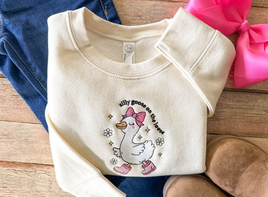 Folded baby sweater with a cartoon goose design on a wooden surface