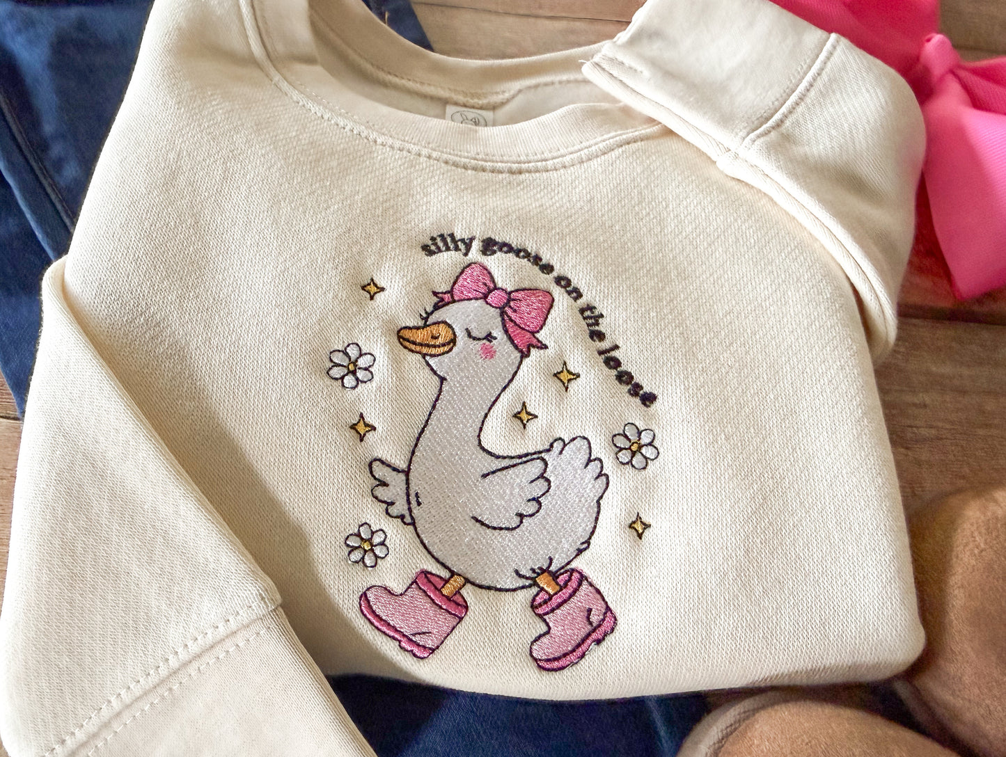 Beige sweatshirt with a cartoon goose design and text on a wooden surface