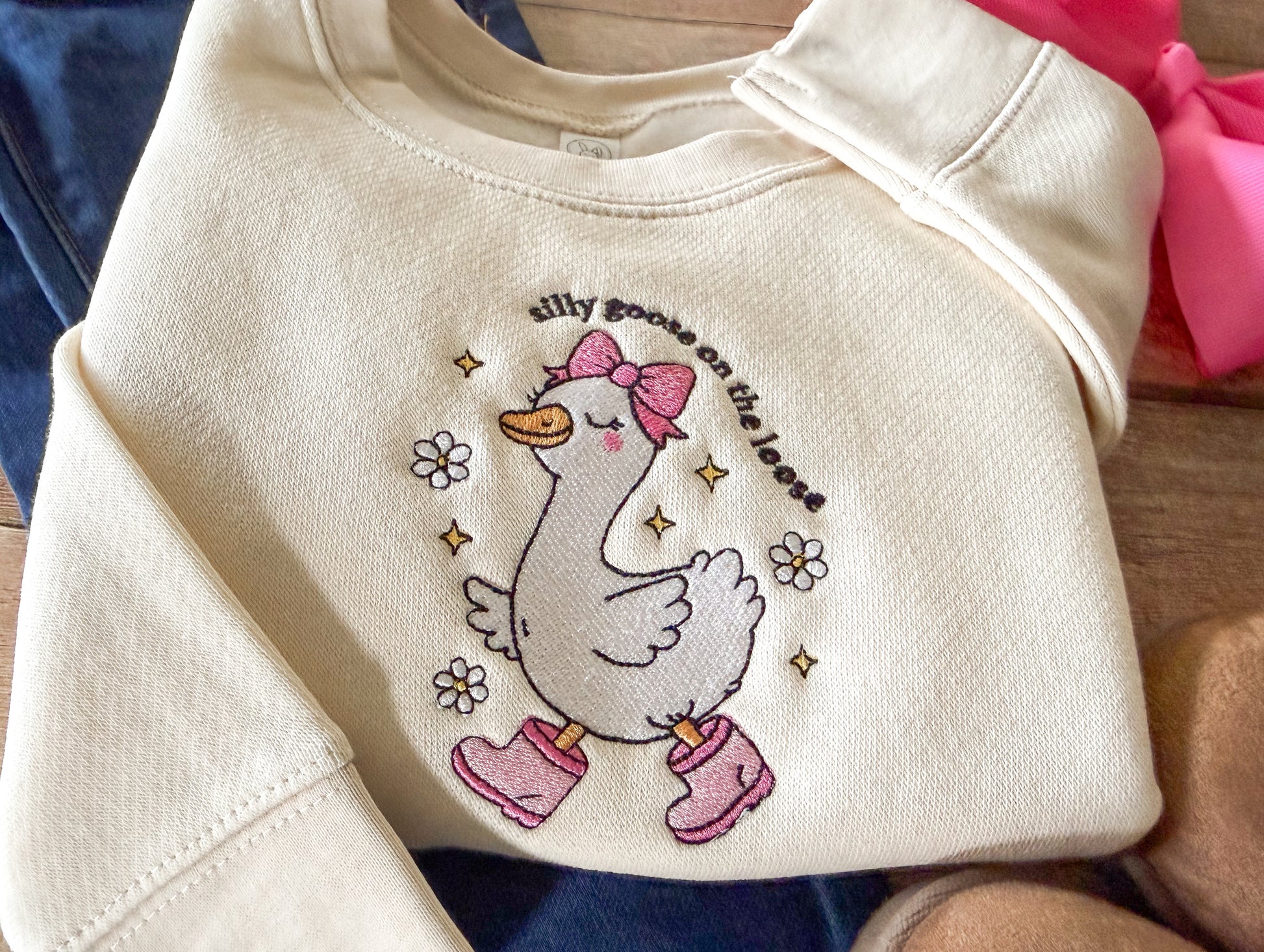 Beige sweatshirt with a cartoon goose design and text on a wooden surface