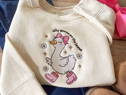 Beige sweatshirt with a cartoon goose design and text on a wooden surface