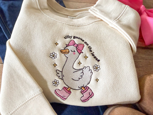 Beige sweatshirt with a cartoon goose design and text on a wooden surface