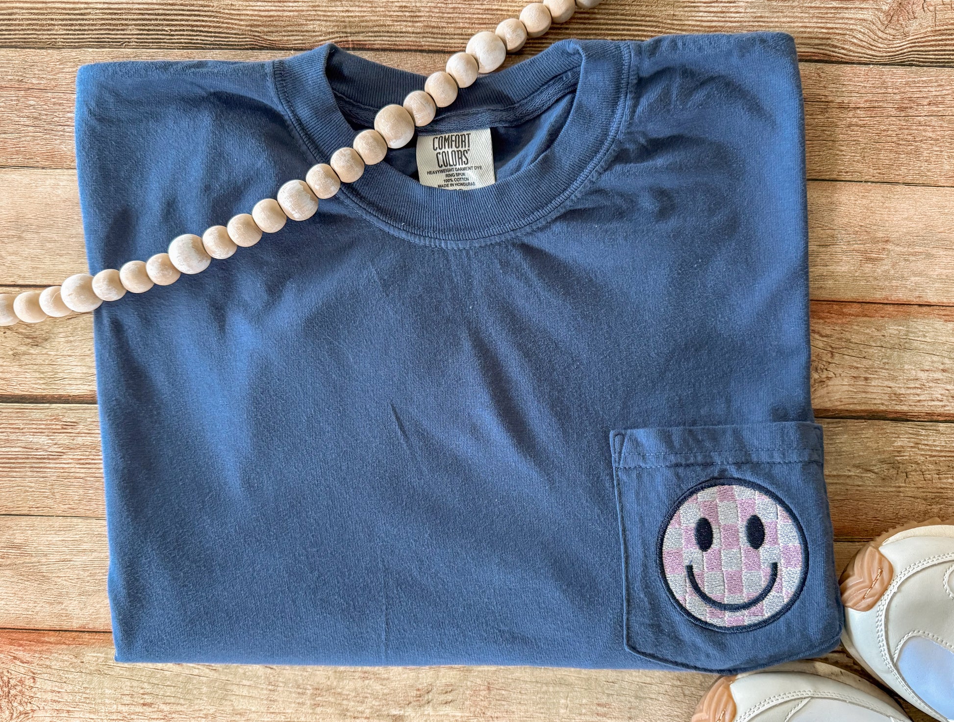 Blue Comfort Colors pocket t-shirt with a smiley face pocket patch on a wooden surface