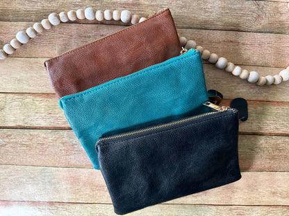Three leather pouches in brown, blue, and black on a wooden surface with a beaded strap.