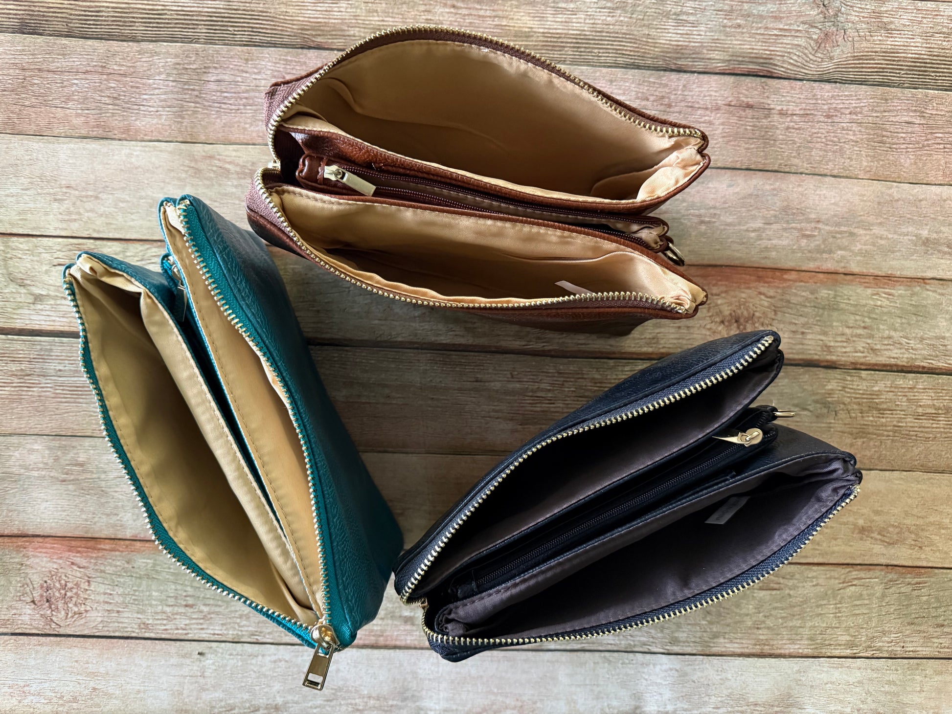 Three open leather bags in teal, brown, and black on a wooden surface