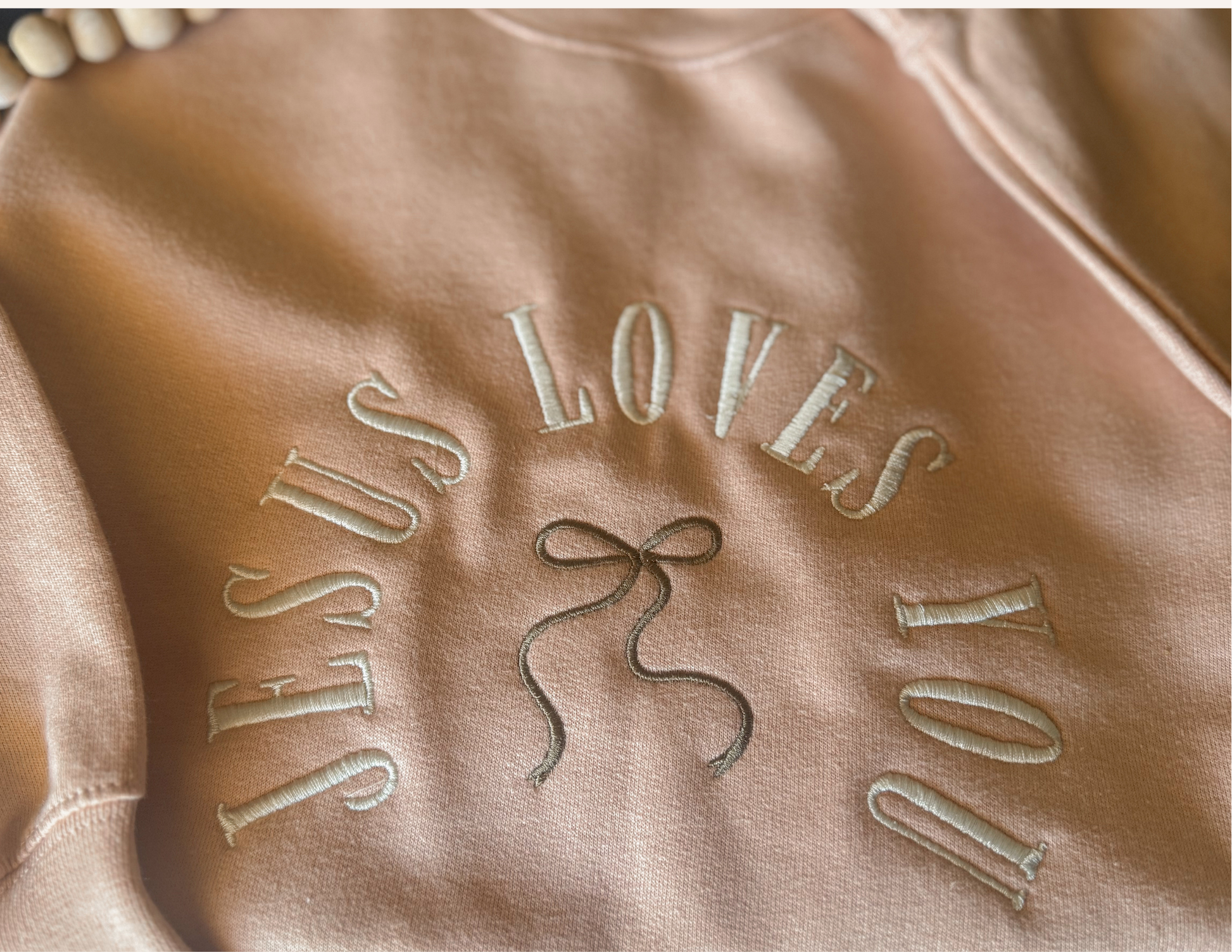 Brown fabric with 'JESUS LOVES YOU' embroidered in white thread.