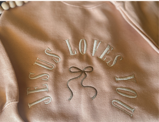 Brown fabric with 'JESUS LOVES YOU' embroidered in white thread.