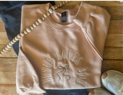 Folded pink sweatshirt with 'Jesus Loves You' text on a wooden surface