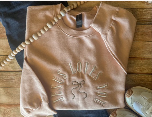 Folded pink sweatshirt with 'Jesus Loves You' text on a wooden surface